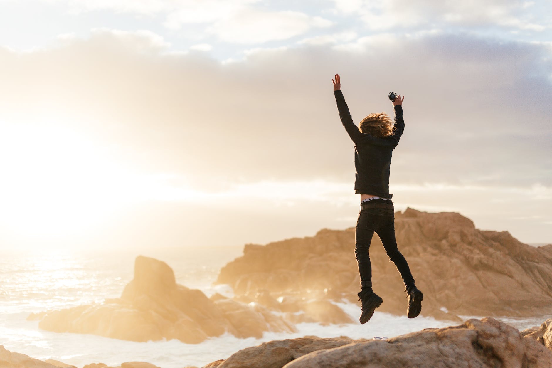 unrecognizable man jumping on stones near sea